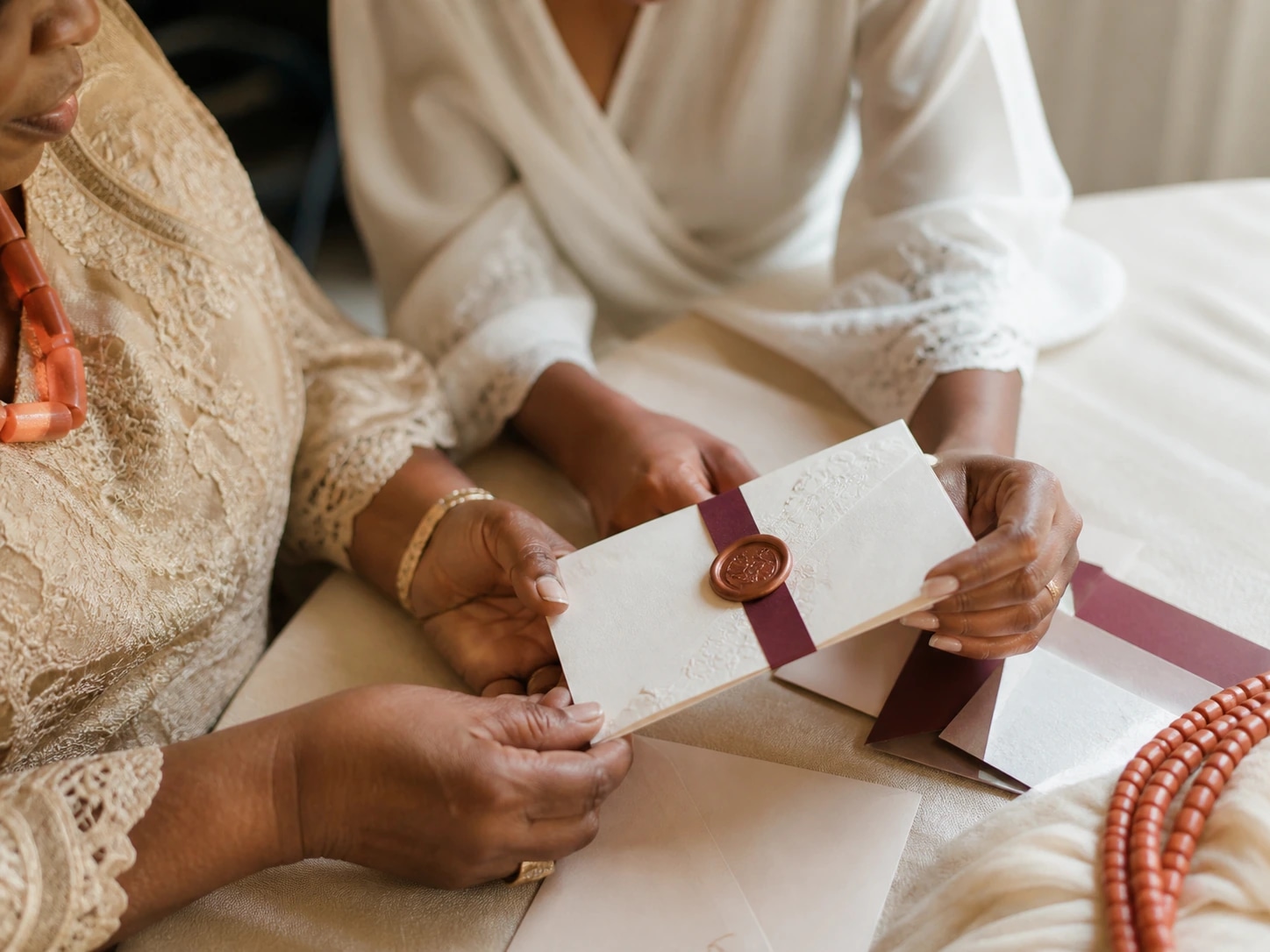 Hands holding an ivory wedding invitation with a burgundy envelope.